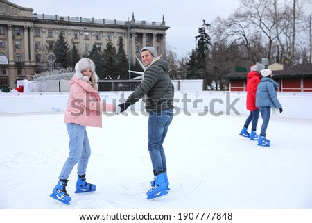 Happy couple skating along ice rink outdoors