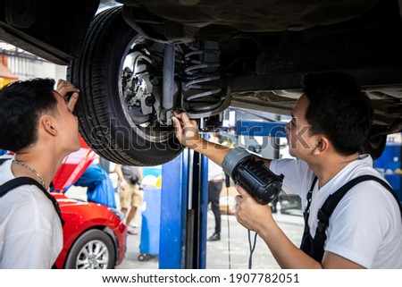 Two mechanic was checking the car suspension. Vehicle raised on lift at maintenance station. Car in service station with two men repair. Car mechanic working at automotive service center. Royalty-Free Stock Photo #1907782051