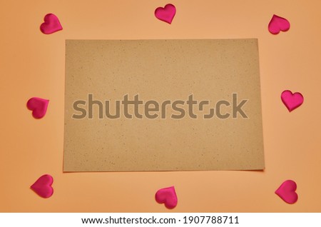 A clean sheet of crafted brown paper rests on a beige background. Frame of red Decorative little hearts. Flat lay. A place to copy.