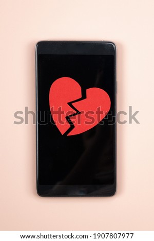 Smartphone with broken red paper heart on it. Parting, unrequited love concept,. High quality photo