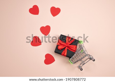 Shopping trolley with gift box, love hearts with copy space on pink background. St. Valentine's Day shopping and sales concept. High quality photo