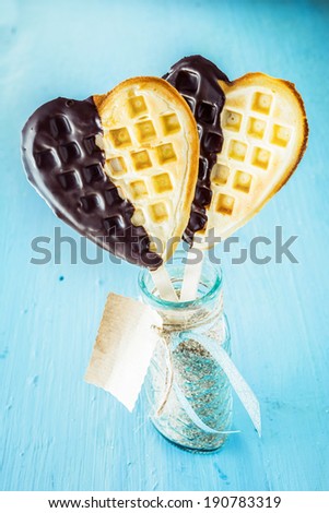 Two romantic heart shaped golden waffles dipped in chocolate symbolic of love on a stick in a glass jar with gift tag for a sweetheart on a special occasion or celebration