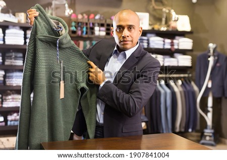 Focused man choosing warm sweater while shopping at apparel shop