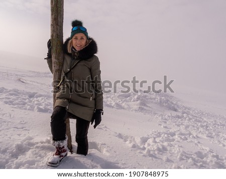 BEAUTIFUL PHOTO OF BLONDE WOMAN LEANING ON A TREE WITH THE SUN AMONG THE FOG WITH EVERYTHING SNOWY AROUND HER