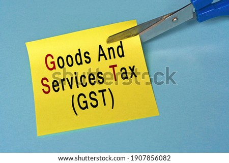 Scissors that cut yellow notepad with goods and services tax text on a blue background. Tax concept