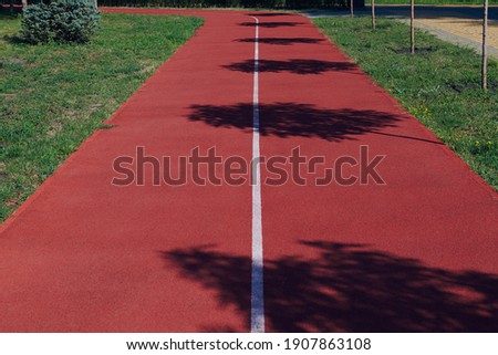 Red rubber jogging track in the park on a sunny day with shadows from trees. Horizontal photo.