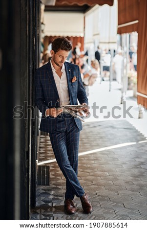 Handsome man in checked suit reading newspaper on the street
