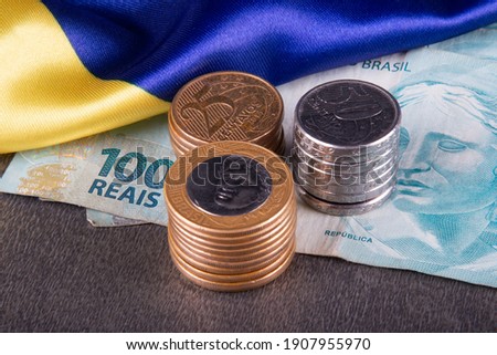 One hundred reais notes and coins over Brazilian flag.