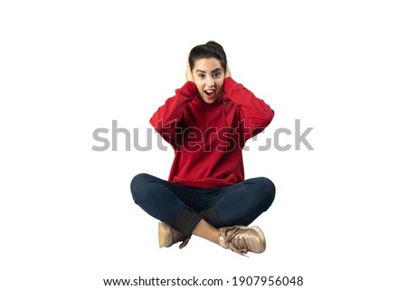 Young beautiful girl is amazed and closed her ears with her hands sitting on an isolated white background