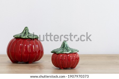 Two pumpkins of different sizes in red color and green cover. Utensil can be used to store rice, beans, flour, pasta, seasoning, food in general. Porcelain decoration accessory for the kitchen.