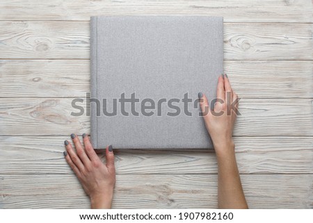 closed grey wedding photo album isolated on wooden background.
person opens a photobook.
womans fingers touch a family photoalbum. womans hand holding beautiful family photo book with space for text