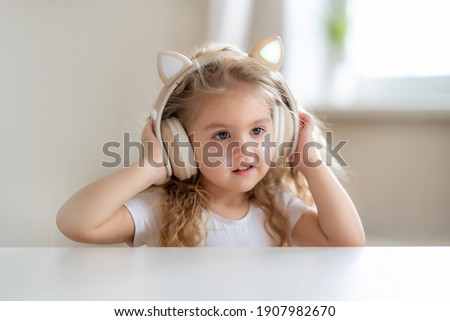 Cute little girl listens to music in children's headphones at home. High quality photo Royalty-Free Stock Photo #1907982670
