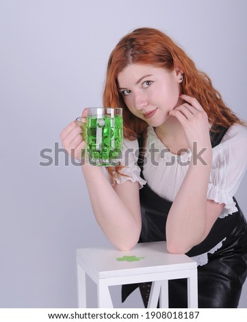 Beautiful woman in dress with glasses of green beer posing on grey background. Happy St. Patrick's Day.