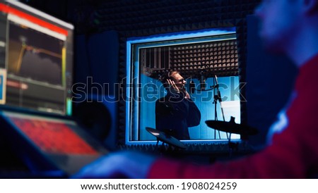 Male Rap Singer with Headphones and Sound Engineer are creating a new song in professional recording studio. Program and tools for creating music on computer monitor. Work in the music recording room Royalty-Free Stock Photo #1908024259