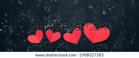 Red paper hearts in a row on a black rustic stone background, banner. Valentine's day. Top view, flat lay
