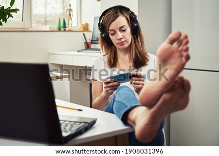 Woman listening online course in the headphones, distance education. Freelancer sitting at workplace and procrastinating. Lazy and distracted employee at remote work