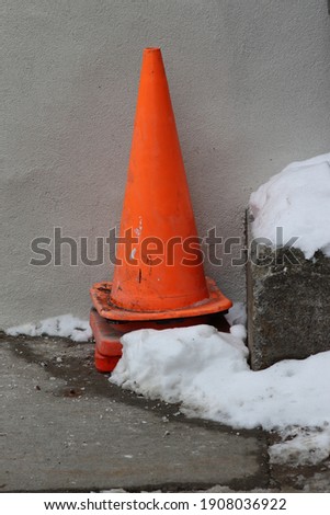 orange cones stacked next to a beige wall with snow
