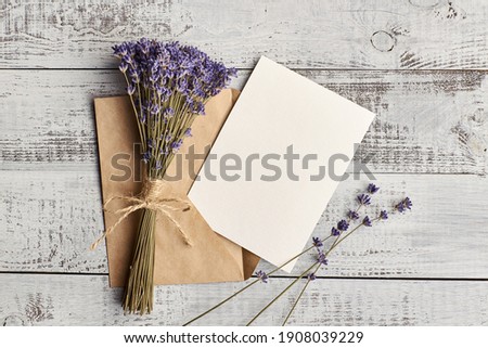 Flat lay with empty greeting card with envelope and dry lavender flowers on wooden background, top view, copy space