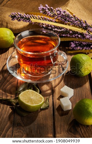 Tea in a white cup next to lime and flowers on a wooden background Royalty-Free Stock Photo #1908049939