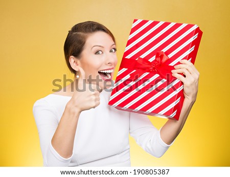 Closeup portrait happy, excited young woman about to open, unwrap red birthday gift box, giving thumbs up isolated yellow background. Positive emotions, facial expression, feelings, attitude, reaction