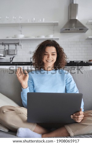Happy hispanic teen girl waving using laptop computer enjoying online virtual chat video call with friends or family in distance e chat virtual meeting using pad computer sitting on sofa at home. Royalty-Free Stock Photo #1908065917
