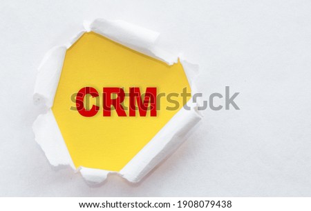 Top view of white torn paper and the text CRM - Customer Relationship Management on a yellow background.