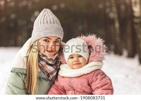 Portrait of a young mother and little daughter in the winter in the woods. A look at the camera
