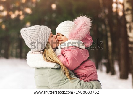 Young mother holds her little daughter in her arms and kisses her. Family portrait. Motherhood and childhood