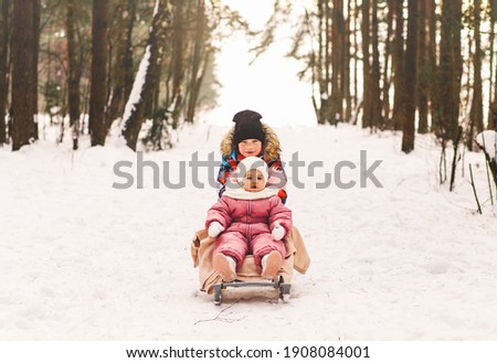 A little boy takes his little sister on a sled in winter.