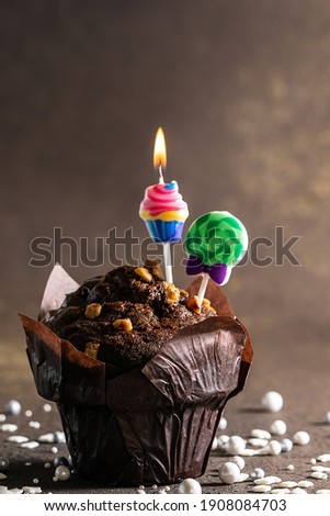 Chocolate cupcake with decorative birthday candles and shining confetti on brown rustic background close up. 