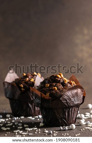 Fresh homemade chocolate muffins on brown rustic background with copy space for your design. Tasty dessert on the table. Vertical image.