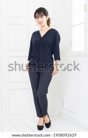 A young woman in dark blue clothes standing in a white room
