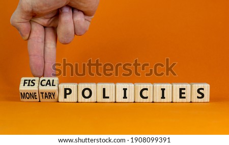 Fiscal or monetary policies symbol. Businessman turns wooden cubes, changes words fiscal policies to monetary policies. Orange background. Business and Fiscal or monetary policies concept. Copy space. Royalty-Free Stock Photo #1908099391