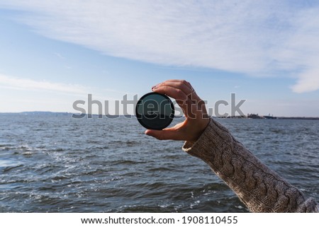 The arm of a woman holding up a lens filter in front of the Statue of Liberty