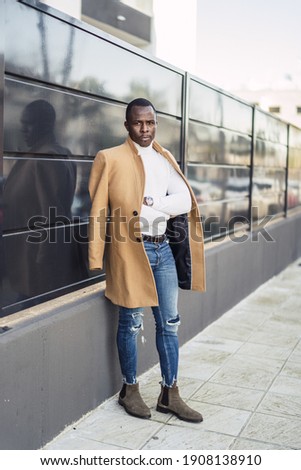 A vertical shot of a stylish handsome African male in a coat posing for the camera