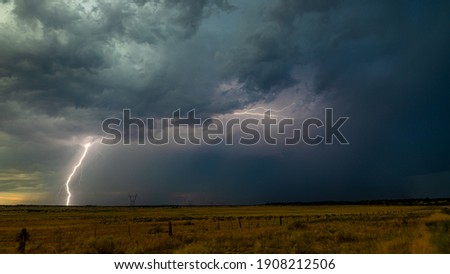 a powerful lightning bolt strikes the ground in an open field below ominous clouds.