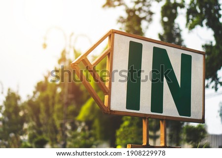 Signboard on the street with "In" text with green background and sunlight. Entrance signboard, street signboard.