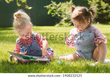 Two little girls sisters paint with finger paints on the street on the grass in summer