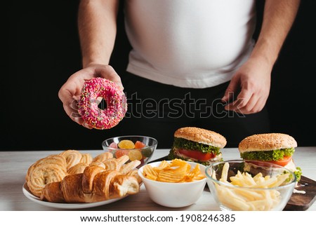 Food addiction, cheat meal, diet breakdown, compulsive overeating concept. Young overweight man fighting the temptation to eat junk food Royalty-Free Stock Photo #1908246385