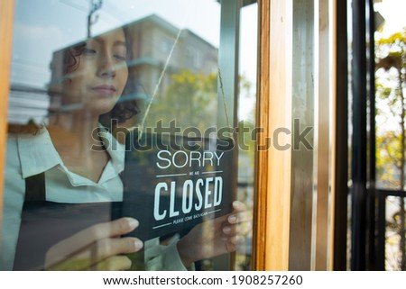Store owner turning close sign wood broad to stop service food and beverage to customer.Asian entrepreneur leaning.Waiter stand and flip advertise hanging in front of coffee shop.