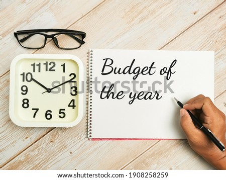 Top view text Budget of the year written on notebook with pen,alarm clock and eye glasses on wooden table. Motivational quote.