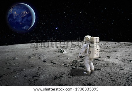 An astronaut standing on the surface of the moon looking up to the earth on the background. Elements of this image furnished by NASA. Royalty-Free Stock Photo #1908333895