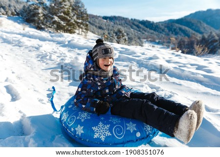 Winter joy and outdoor actovity in snowly forest in mountains. Child boy enjoying tubing ride on snow hill
