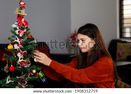 Portrait of a beautiful young girl decorating a Christmas tree at home, celebrating festival.