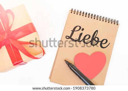 Valentine's day concept. Creaft gift box with red ribbon,pink wooden heart,black marker and craft colour notepad with LIEBE sign