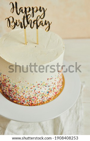 A vertical shot of a cake with a ''happy birthday'' cake topper and sprinkles on a tray