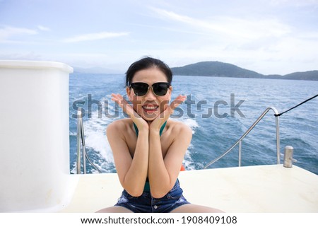 Portrait of Asia beautiful young woman at yacht deck on the background of ocean trace, blue cloudy sky and mountain. Cheerful.
