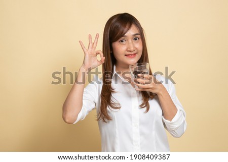 Young Asian woman show OK with a glass of drinking water on beige background