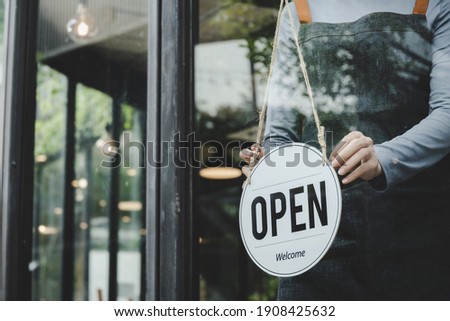 asian waitress staff woman wearing apron turning open sign board on glass door in modern cafe coffee shop, hotel, cafe restaurant, retail store, small business owner, food and drink concept
