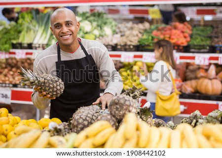 Portrait of latino-american worker in supermarket with pineapples Royalty-Free Stock Photo #1908442102
